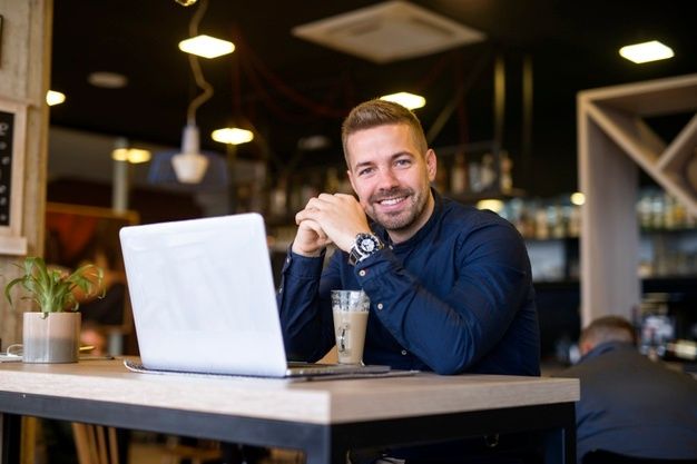Portrait of smiling man sitting in a cafe bar with his laptop computer _ Free Photo